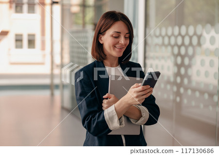 A young professional woman is seen using a smartphone in a modern office setting 117130686