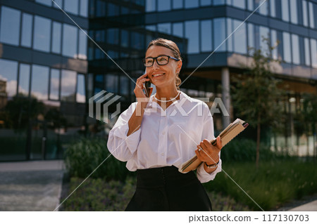 A professional woman dressed in business attire is actively engaging in a phone call 117130703