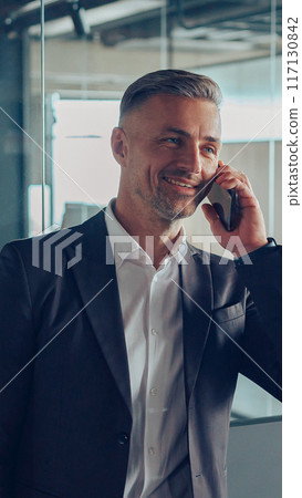 Handsome male manager in business casual clothes is talking phone with client at office Handsome male manager in business casual clothes is talking phone with client at office 117130842
