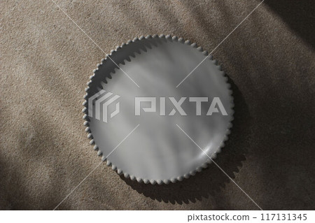 Summer restaurant still life scene. Blank white ceramic plate with decorative bobbin rim in sunlight on beige lime stone floor, table background. Mediterranean flat lay, top view. Moody shadows, light 117131345