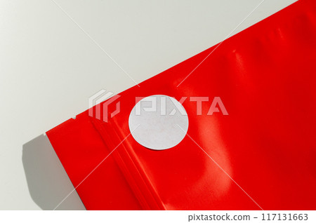 White circular sticker on red poly mailer envelope with natural shadow. 117131663