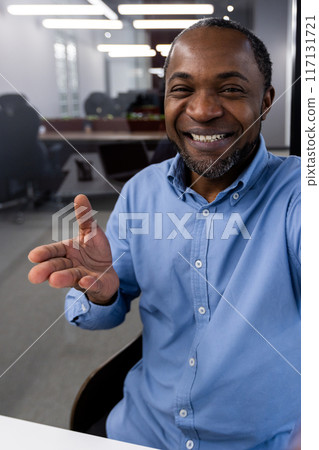 Smiling man making a video call in modern office environment, engaging in remote conversation. Demonstrating casual and friendly communication, using phone for video chat and interactive discussion. Smiling man making a video call in modern office environment, engaging in remote conversation. Demonstrating casual and friendly communication, using phone for video chat and interactive discussion. 117131721