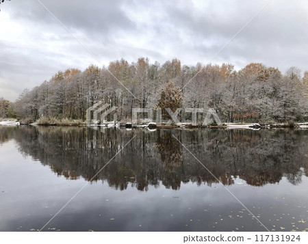 Beautiful landscape by the river, late autumn, early winter, trees dusted with the first snow reflected in the river 117131924