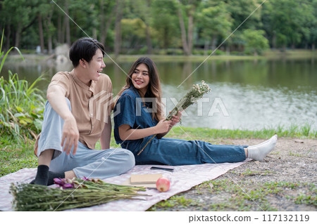 Young Couple Enjoying a Relaxing Picnic by the Lake in a Serene Park Setting 117132119