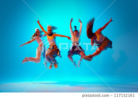 Dancers dressed casual attire leaping in motion, performing dance moves in mid-air in vibrant neon light against gradient studio background. Dancers dressed casual attire leaping in motion, performing dance moves in mid-air in vibrant neon light against gradient studio background. 117132161