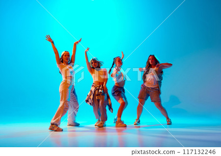 Group portrait of dancers performing contemp moves in motion in vibrant neon light against gradient blue studio background. 117132246
