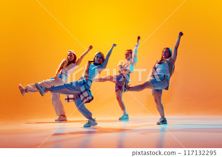 Group of female dancers, friends in retro fashion attire dancing in motion in vibrant neon light against gradient studio background. 117132295
