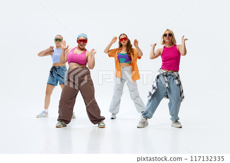 Diverse group of female dancers in vibrant streetwear and sunglasses training dance moves energetically against white background. Diverse group of female dancers in vibrant streetwear and sunglasses training dance moves energetically against white background. 117132335