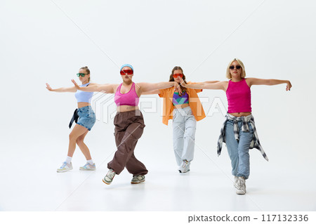 Diverse group of four dancers in vibrant streetwear and sunglasses moves in dance energetically against white studio background. 117132336