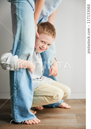 Hyperactive kid holding his mother's legs. Clingy son wanting attention from mommy. Young boy hugging mom's legs and smiling to camera. 117133068