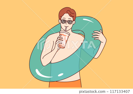 Man goes to beach and drinks cold cocktail, holding inflatable swimming ring in hand 117133407
