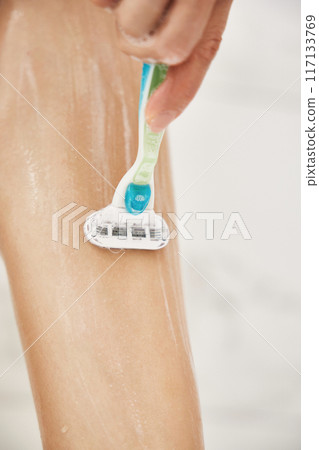 Young woman shaving her legs with razor in white shower, close-up 117133769