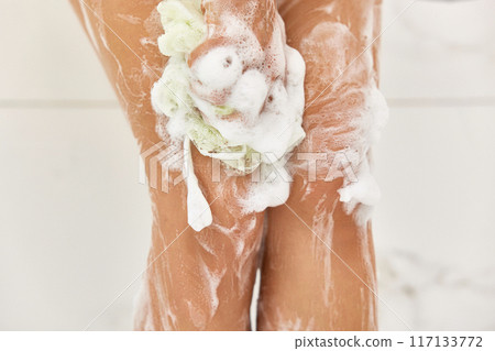 Woman washing her legs with foam bubbles and bath sponge while taking shower in the bathroom 117133772