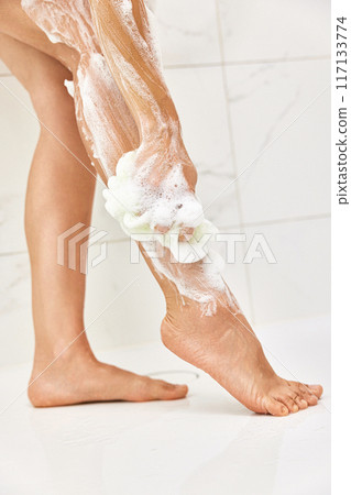 Woman washing her legs with foam bubbles and bath sponge while taking shower in the bathroom Woman washing her legs with foam bubbles and bath sponge while taking shower in the bathroom 117133774