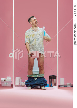 Man wearing tropical shirt standing in toilet, holding toilet brush and tablet, watching game translation and singing against pink background Man wearing tropical shirt standing in toilet, holding toilet brush and tablet, watching game translation and singing against pink background 117134189
