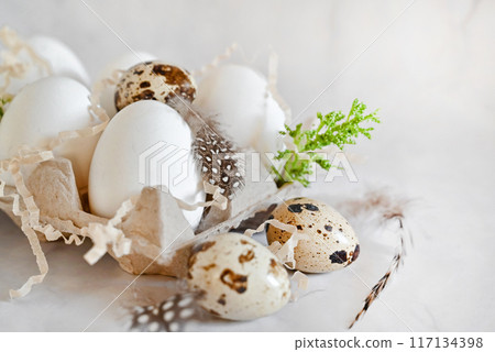 Easter eggs on rustic table with cherry blossoms. Happy Easter. Natural dyed colorful eggs in paper tray with linen napkin and spring flowers in rustic room. Countryside still life Easter eggs on rustic table with cherry blossoms. Happy Easter. Natural dyed colorful eggs in paper tray with linen napkin and spring flowers in rustic room. Countryside still life 117134398
