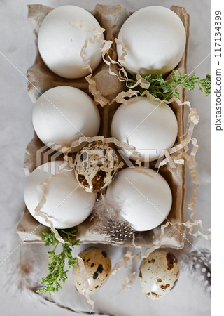 Easter eggs on rustic table with cherry blossoms. Happy Easter. Natural dyed colorful eggs in paper tray with linen napkin and spring flowers in rustic room. Countryside still life Easter eggs on rustic table with cherry blossoms. Happy Easter. Natural dyed colorful eggs in paper tray with linen napkin and spring flowers in rustic room. Countryside still life 117134399