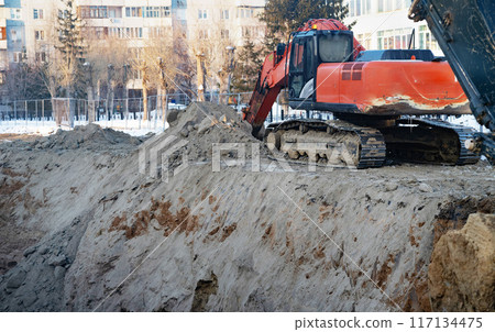 Excavator during earthmoving at open pit on blue sky background. Construction machinery and earth-moving heavy equipment for excavation, loading, lifting and hauling of cargo on job sites 117134475