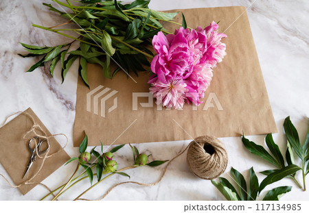 A female florist makes a bouquet of peony flowers wrapped in kraft paper on her desktop. View from above. High quality photos A female florist makes a bouquet of peony flowers wrapped in kraft paper on her desktop. View from above. High quality photos 117134985
