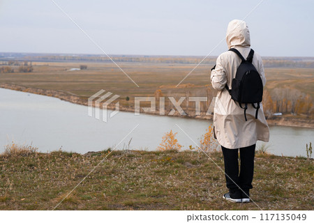 A woman stands on the edge of a cliff and looks at a nearby island, the sea. Unity with nature. A woman stands on the edge of a cliff and looks at a nearby island, the sea. Unity with nature. 117135049