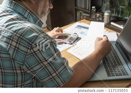 White man sitting with a sheet in his hands reviewing cash and money flows, projections and bills. Concept work at home, checking accounts, economy of the home. View to normal. 117135055