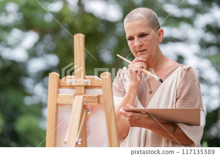 Thoughtful Artist Contemplating Her Work While Holding a Paintbrush and Palette Outdoors Thoughtful Artist Contemplating Her Work While Holding a Paintbrush and Palette Outdoors 117135389