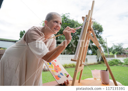 Woman Enjoying Outdoor Painting Session on a Sunny Day with Easel and Palette in a Garden Setting Woman Enjoying Outdoor Painting Session on a Sunny Day with Easel and Palette in a Garden Setting 117135391