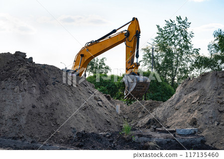 Excavator during earthmoving at open pit on blue sky background. Construction machinery and earth-moving heavy equipment for excavation, loading, lifting and hauling of cargo on job sites 117135460