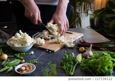 A woman cuts fresh cauliflower at the table A woman cuts fresh cauliflower at the table 117136112