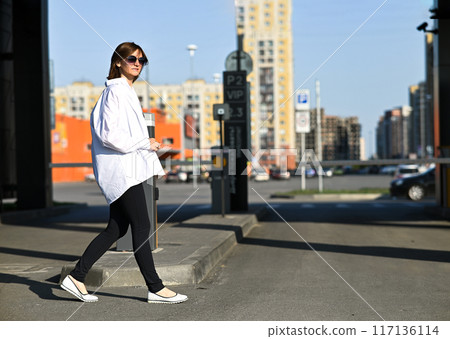 Young woman in formal clothes walking near grey wall outdoors, space for text 117136114