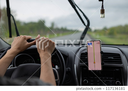 Rear view of a young traveler using a navigator on a mobile phone behind the wheel of a modern car . Rear view of a young traveler using a navigator on a mobile phone behind the wheel of a modern car . 117136181