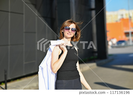 Confident young girl in a white t-shirt and sunglasses walks through the city streets enjoying a summer day. Street photography 117136196