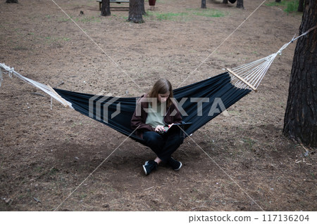 A girl in a hammock is working on a computer A girl in a hammock is working on a computer 117136204