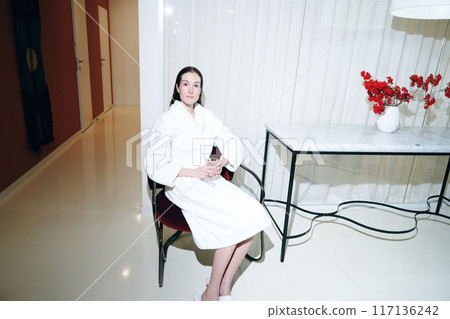 Relaxed Woman in a Bathrobe Sitting in a Bright Modern Room With Decorative Flowers Relaxed Woman in a Bathrobe Sitting in a Bright Modern Room With Decorative Flowers 117136242