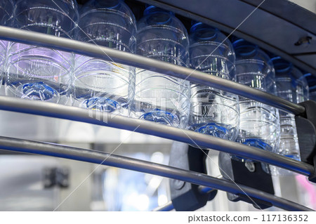 The  empty drinking water bottles  hanging on the conveyor belt for filling process. 117136352