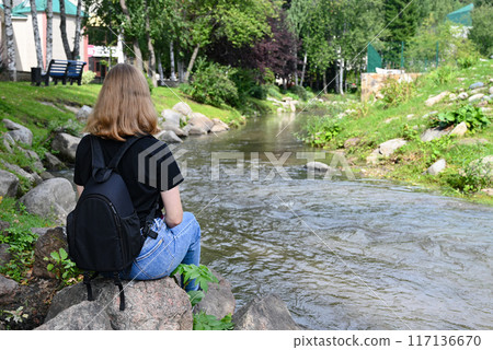 A young lady is sitting on large rocks next to a mountain river. A young lady is sitting on large rocks next to a mountain river. 117136670