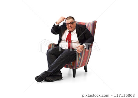 Overweight businessman in formal wear, red tie and glasses, sitting in armchair and emotionally talking, discussing news isolated on white background. Overweight businessman in formal wear, red tie and glasses, sitting in armchair and emotionally talking, discussing news isolated on white background. 117136808