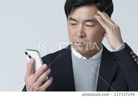 一名 50 多歲的男子看著他的智慧型手機，做出消極的表情 117137149