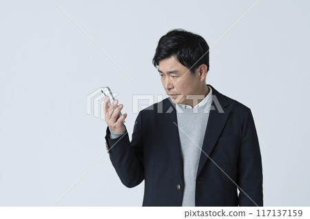 一名 50 多歲的男子看著他的智慧型手機，做出消極的表情 117137159