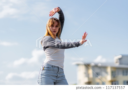 Young Dancer Engaging in Expressive Movement Against a Clear Sky in Urban Environment 117137557