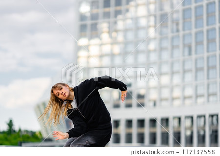 Young Dancer Performing Urban Dance Routine at Modern Cityscape During Overcast Afternoon Young Dancer Performing Urban Dance Routine at Modern Cityscape During Overcast Afternoon 117137558