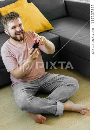 Young man spending time at home, sitting on a floor in apartment and playing arcade car video games on console. Male using controller to play street racing drift simulator. Young man spending time at home, sitting on a floor in apartment and playing arcade car video games on console. Male using controller to play street racing drift simulator. 117137825