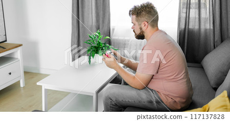 Banner man spending time at home, sitting on a couch in apartment and playing arcade car video games on console copy space. Male using controller to play street racing drift simulator. Banner man spending time at home, sitting on a couch in apartment and playing arcade car video games on console copy space. Male using controller to play street racing drift simulator. 117137828