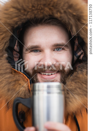 Close-up portrait handsome bearded millennial man in winter clothes and with thermos snow outdoor. Cold season and hot beverage in winter time Close-up portrait handsome bearded millennial man in winter clothes and with thermos snow outdoor. Cold season and hot beverage in winter time 117138750
