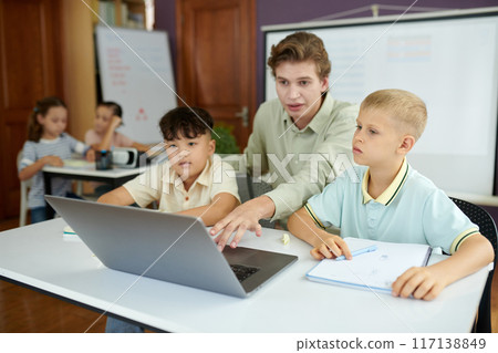 Educator Guiding Students in Classroom with Laptop 117138849