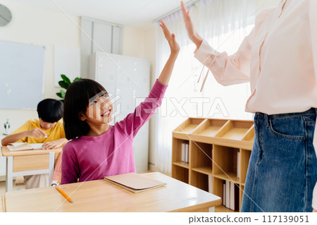 Joyful Asian primary student celebrating achievement with teacher through energetic high-five Joyful Asian primary student celebrating achievement with teacher through energetic high-five 117139051
