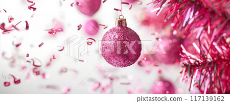 Shiny pink Christmas ornament hanging on pink tree with confetti, background 117139162