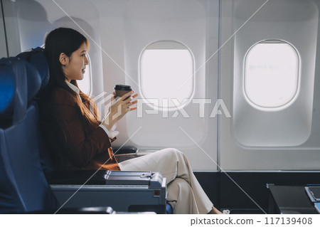 A female tourist is sitting inside a passenger plane, looking at the bird's eye view from the airplane window. A female tourist is sitting inside a passenger plane, looking at the bird's eye view from the airplane window. 117139408