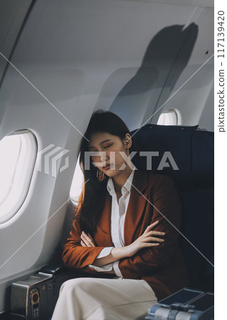 Photo of a frustrated woman sitting on an airplane with her head in her hands. Asian woman sitting in a seat in airplane 117139420