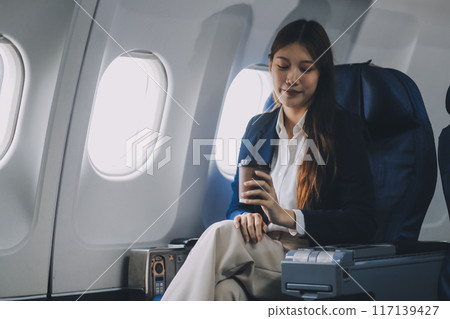 Young Asian female tourist traveling alone on a plane is drinking hot coffee and looking out the window. 117139427